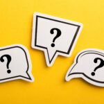 Three white speech bubble cutouts with black question marks on a bright yellow background, symbolizing questions, inquiry, or the search for information.