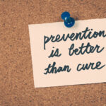 A handwritten note pinned to a corkboard with a blue pushpin reads "prevention is better than cure," conveying an important message about the value of proactive measures in health and wellness.