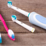 Three toothbrushes, two manual with pink and blue handles and one electric with a white and blue handle, lying on an old wooden surface, depicting dental care tools.