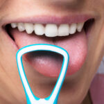 A woman is smiling while sticking out her tongue for tongue scraping to help improve her oral health.