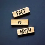 Three wooden blocks arranged vertically on a dark background. The top block reads "FACT," the middle one says "VS," and the bottom block says "MYTH." The words are printed in bold black letters, representing the contrast between fact and myth.