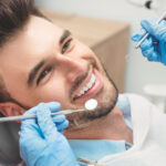Smiling man reclining in a dental chair while a dentist examines his teeth with mirror and probe